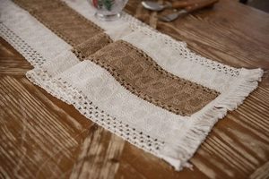 Detail of woven table runner with cotton linen fabric and tassel trim on wood table