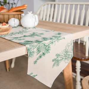 Linen table runner with green pine and holly print on a light wooden dining table