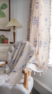 Close-up of beige cotton linen curtain featuring blue floral prints and tassel fringe detail