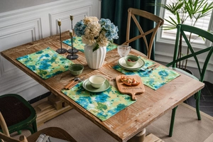 Close-up of abstract watercolor place mats in green and blue on a rustic wooden dining table