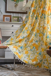 Detail view of yellow floral curtains with delicate white pom-pom fringe in a cozy room