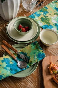 Detailed view of Morandi green ceramic dinnerware with rustic linen placemats and cutlery