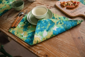 Detail of green tie-dye camo placemat with linen texture on a wooden dining table