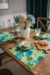 Detailed view of tie-dye green and blue cotton linen placemats on a rustic wooden dining table