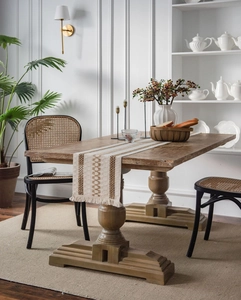 Detail of a beige striped cotton linen table runner with fringes on a rustic wooden dining table