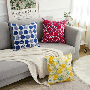 Three decorative floral and geometric square pillow covers on a modern grey sofa