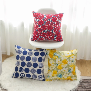 Three decorative floral print pillow covers on a white chair in a bright, cozy living room
