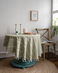 Détails de broderie ondulée et pompons crème sur nappe en coton et lin vert herbe