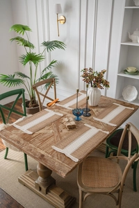 Close-up of woven jute place mat with striped fringe detail on a wooden dining table