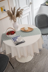Close-up of beige round tablecloth with fringes and grey-green herringbone table runner