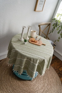Détail d'une nappe ronde verte avec broderies blanches et glands à franges de couleur crème
