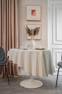 Detail of cream-white round tablecloth with cotton fringe and grey-green runner