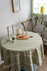 Vue détaillée de la nappe ronde verte avec motif de losanges et bords à franges crème