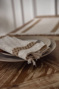 Close-up of cream linen place mat with brown woven stripes and delicate fringe details