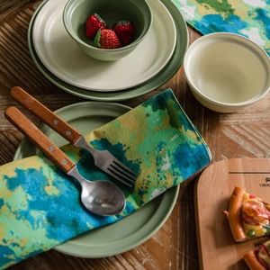Green ceramic dinnerware set with cotton linen placemat on a rustic wooden table