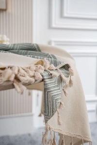 Detailed close-up of beige and green geometric woven tablecloth with tassel fringe