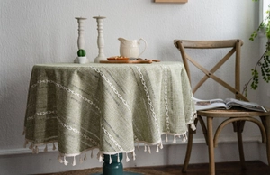Détail de la nappe ronde verte en lin avec broderie géométrique et pompons beiges