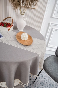 Detail of grey jacquard tablecloth with geometric patterns and white cotton tassels