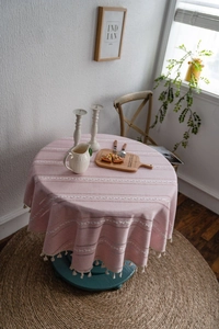 Détail d'une nappe ronde rose avec broderie blanche et bordures à pompons crème