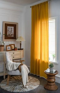 Detail of bright yellow cotton linen curtain featuring white pom-pom trim for boho home decor