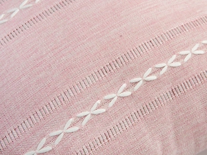 Close-up of pink fabric texture with white cross embroidery and ladder stitch details