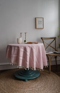 Détail d'une nappe ronde rose en coton et lin avec broderie géométrique et pompons blancs