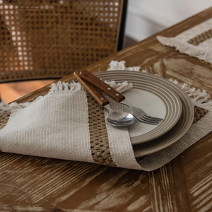 Striped cotton linen placemat with fringe on a wooden table with ceramic dinnerware