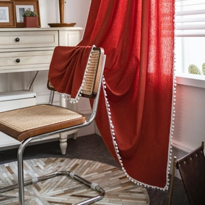 Detail of red textured fabric curtain featuring white pom-pom trim for home decor