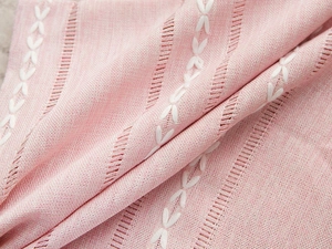Detailed macro view of pink linen fabric with white flower embroidery and hollow design