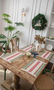 Detail of red and green woven Christmas placemat with tassels on a wooden dining table