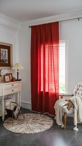 Detail of red linen curtain featuring white pom-pom trim and elegant silver metal rod