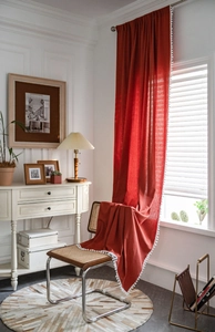 Detail of red linen blend curtain featuring decorative white pom-pom trim for home decor
