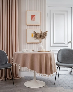 Close-up of beige round tablecloth featuring knit texture and elegant fringe tassels