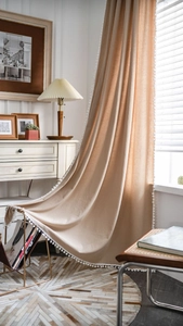Close-up of beige cotton linen curtain with white pom-poms on a magazine rack
