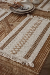 Detail of woven table mat with cream tones, dark stripes and bohemian tassel edges