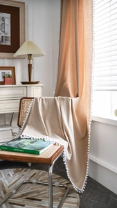 Close-up of beige linen curtain with white pom-pom trim detail in natural light