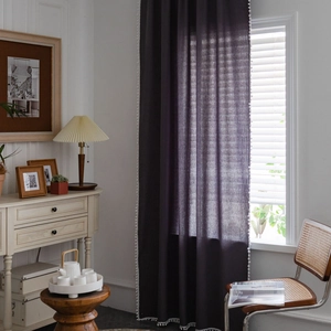 Detail view of dark linen curtain featuring decorative white pom-pom fringe edging