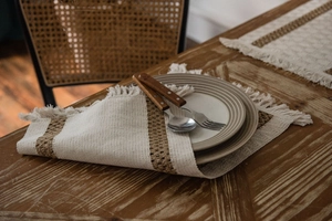 Close-up of woven fringe placemats with hollow brown stripes and ceramic plates set