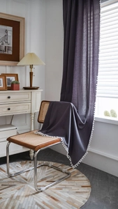 Detail of dark grey linen curtains with white pom-pom trim draped over a chair