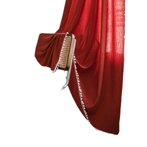 Solid red semi-sheer curtain with white pom-pom trim draped on a vintage chair