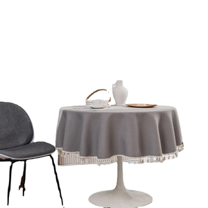 Gray round cotton linen tablecloth with cream tassels on a white round dining table