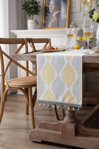 Detail of yellow and grey leaf jacquard table runner with beaded fringe on wood table