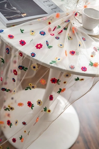 Detailed macro view of colorful floral embroidery on white lace mesh tablecloth fabric