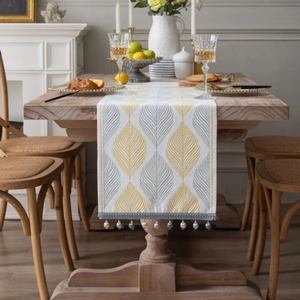 Modern table runner with yellow leaf patterns and beaded tassels on a wooden dining table