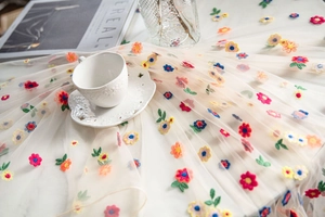 Detailed macro view of colorful floral embroidery on ivory translucent lace tablecloth