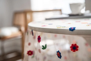 Close-up of white mesh lace tablecloth with colorful floral embroidery details