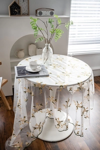 Detail of sheer mesh tablecloth featuring yellow flower embroidery and wavy scalloped edge