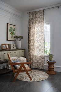 Detail of floral print curtain with black tassel fringe in a cozy vintage farmhouse setting