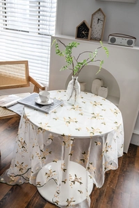 Detail of white mesh lace tablecloth with yellow floral embroidery and green wavy edges