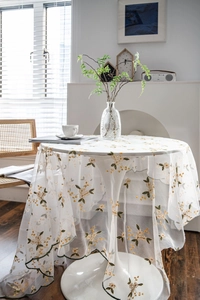 Close-up of white lace tablecloth with yellow flower embroidery and green wavy edges